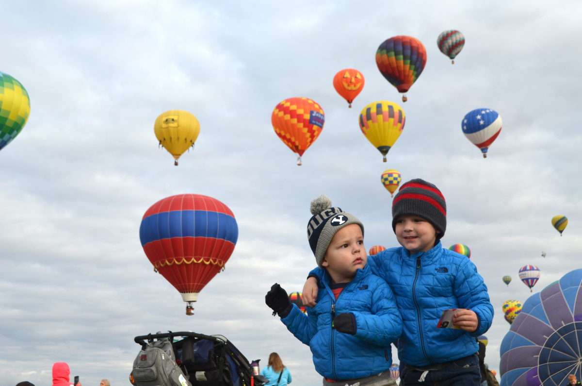 Two young kids pose for a picture in front of a dozen hot air balloons at the Albuquerque International Balloon Fiesta.