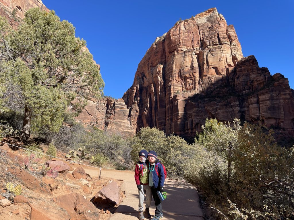 Two boys on the West Rim Trail out to Angel's Landing. The rock formation looms in the background. - Where to Hike in Zion National Park with Kids - Exploring Through Life